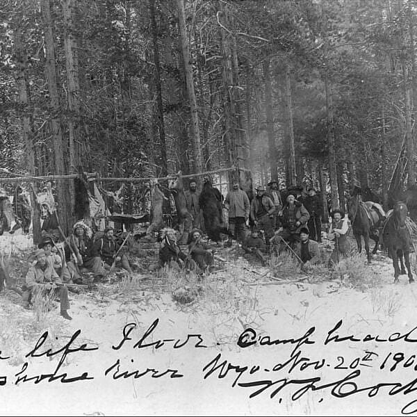William F. Cody, Chief Iron Tail, and Mike Russell (lower left front) with a hunting party of Native American and European American men holding rifles in a snow covered wooded area. Handwritten caption, "The life I love. Camp head of Shoshone river Wyo. Nov. 20th 1901. W. F. Cody." MS 6 William F. Cody Collection. P.69.1062