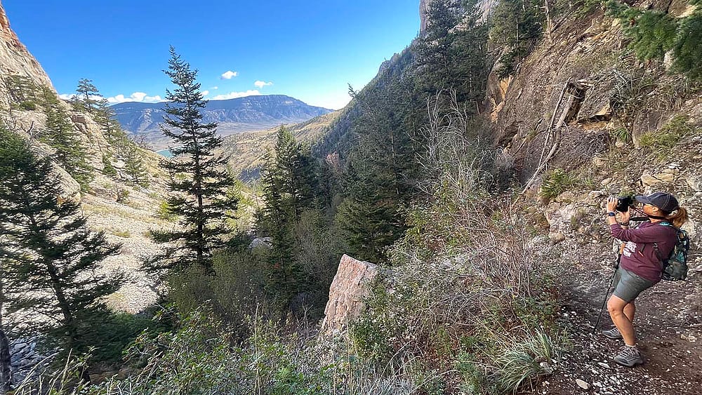 A hiker stops along a trail to take a photograph of the landscape