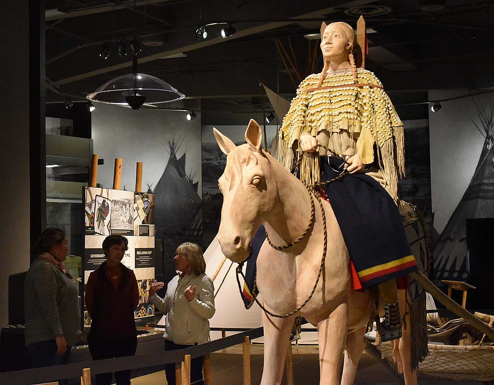 A small tour group views an exhibit of a horse and rider in the Cheyenne Migration gallery of the Plains Indian Museum.