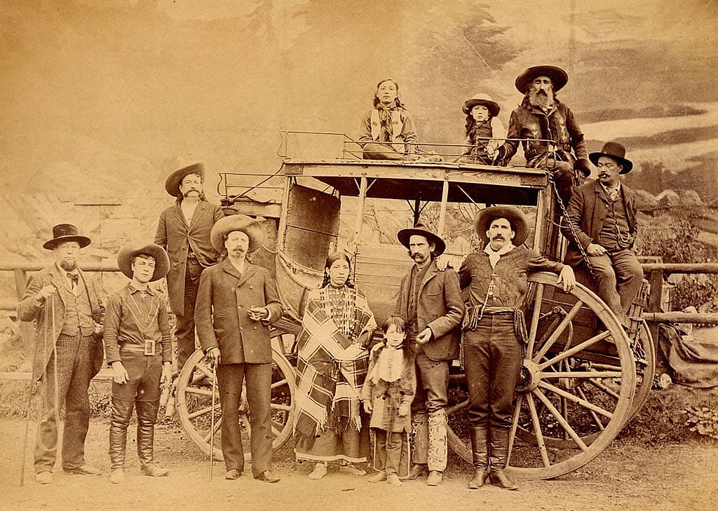 Numerous Wild West personnel with Deadwood stagecoach, ca. 1889. Buffalo Bill stands in front of the smaller wagon wheel with Major Burke behind his right shoulder. MS6 William F. Cody Collection, McCracken Research Library. P.69.2041.1