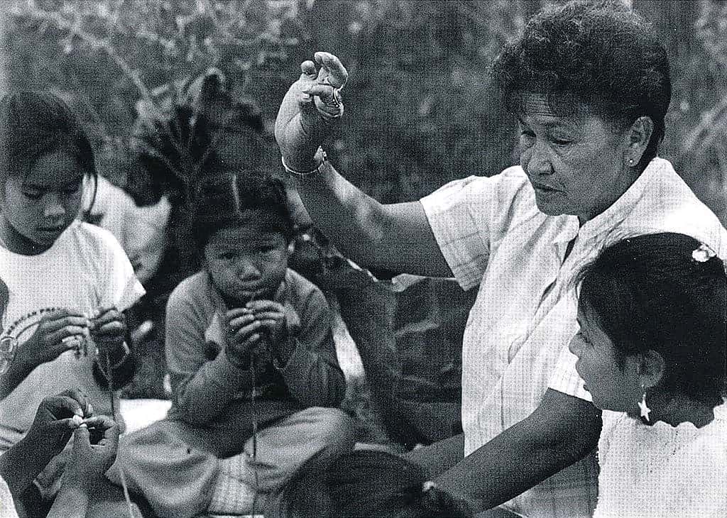Marie Willow teaches a group of girls how to string beads at the 1988 Arapaho Language and Culture Camp sponsored by the Northern Arapaho Tribe and the Wyoming Council for the Humanities. Marie was born May 2, 1939, in the St. Stephens area. Her Arapaho name is Neehii3ei'tou' or "Hits in the Middle." Sara Wiles photo, 1988.