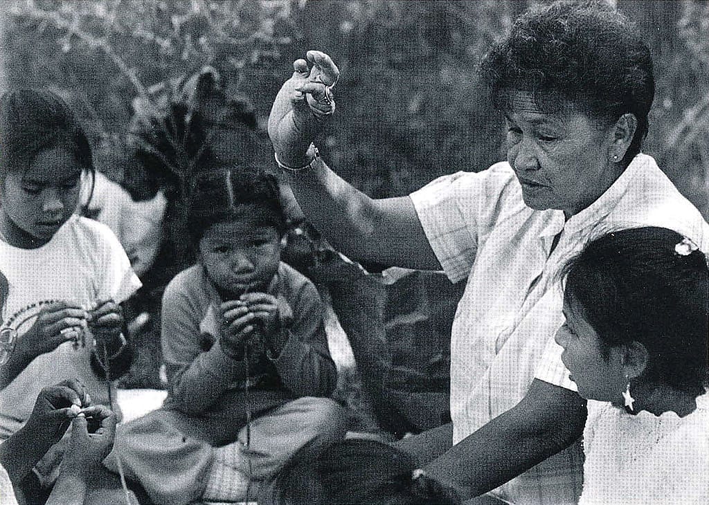 Marie Willow teaches a group of girls how to string beads at the 1988 Arapaho Language and Culture Camp sponsored by the Northern Arapaho Tribe and the Wyoming Council for the Humanities. Marie was born May 2, 1939, in the St. Stephens area. Her Arapaho name is Neehii3ei'tou' or "Hits in the Middle." Sara Wiles photo, 1988.
