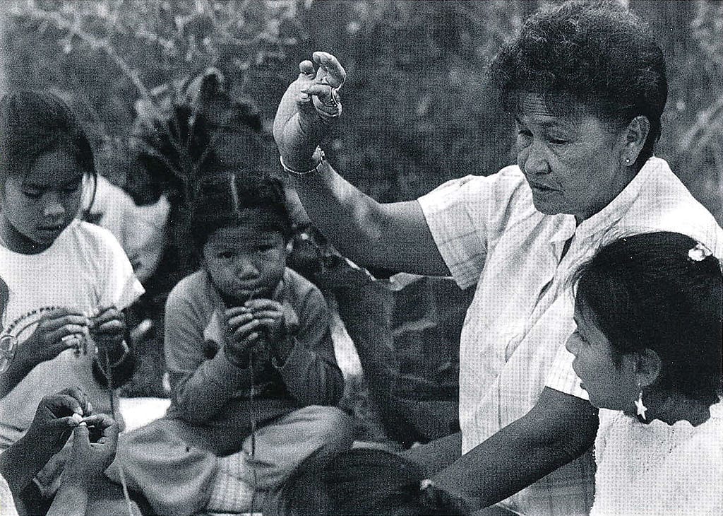 Marie Willow teaches a group of girls how to string beads at the 1988 Arapaho Language and Culture Camp sponsored by the Northern Arapaho Tribe and the Wyoming Council for the Humanities. Marie was born May 2, 1939, in the St. Stephens area. Her Arapaho name is Neehii3ei'tou' or "Hits in the Middle." Sara Wiles photo, 1988.