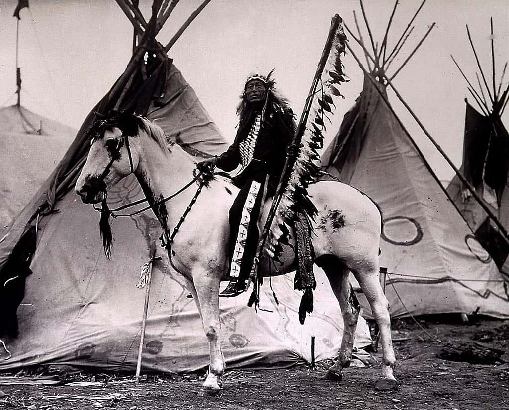 Iron Tail on his horse with tipis. Iron Tail became a close friend of Cody's, performing with the Wild West as well as accompanying him on hunts and other pleasure trips. MS 71 Vincent Mercaldo Collection. P.71.658