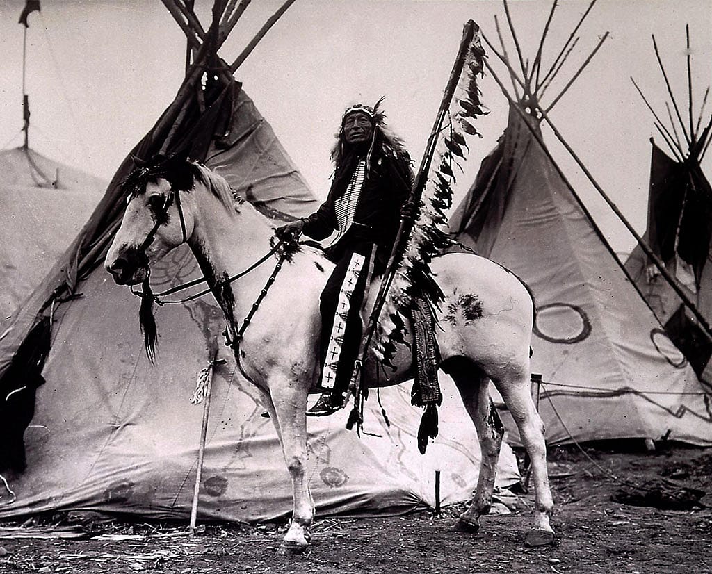 Iron Tail on his horse with tipis. Iron Tail became a close friend of Cody's, performing with the Wild West as well as accompanying him on hunts and other pleasure trips. MS 71 Vincent Mercaldo Collection. P.71.658