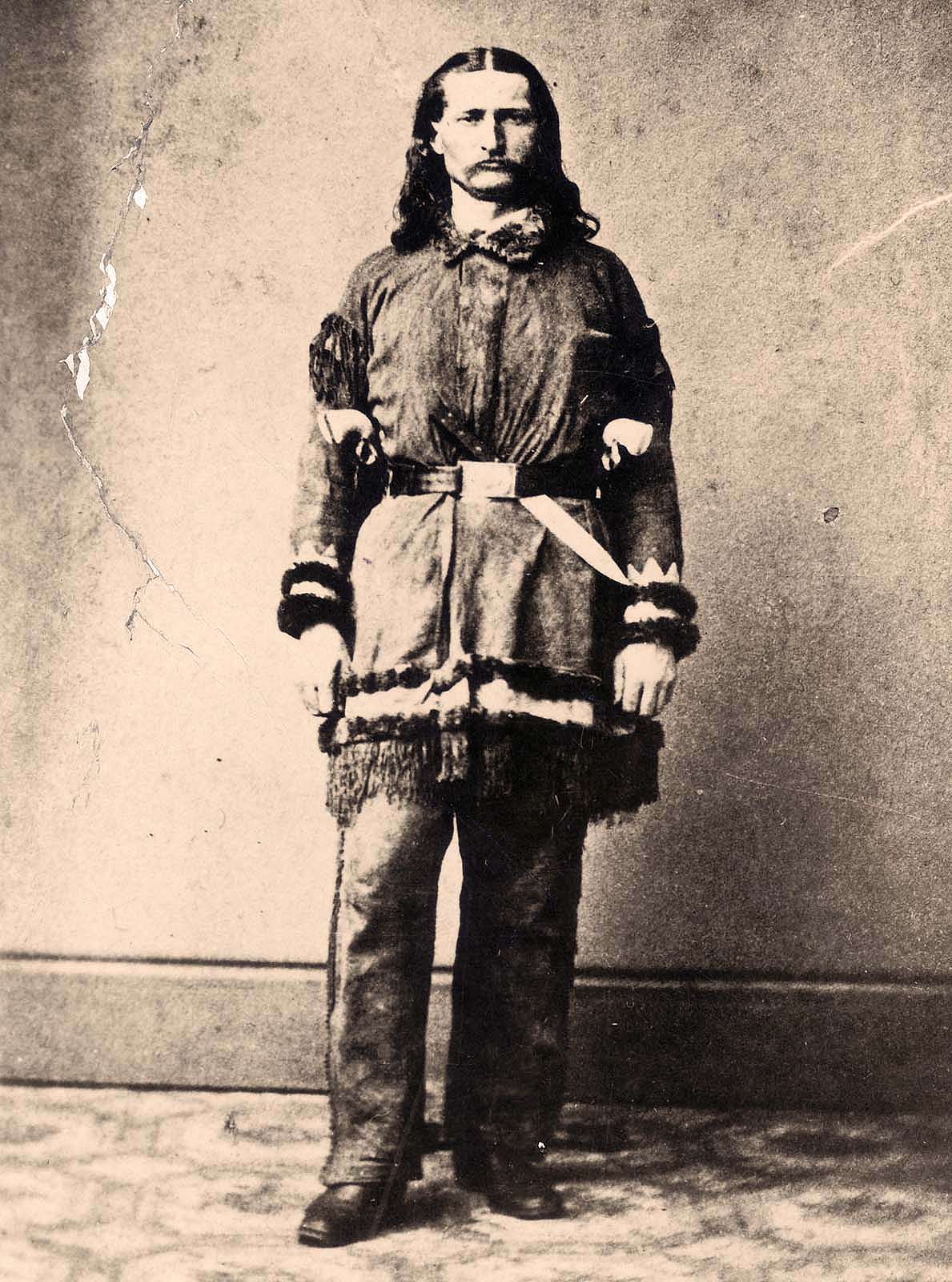 Portrait of James Butler “Wild Bill” Hickok wearing buckskin clothing and standing in front of wall. Knife tucked in belt. MS 71 Vincent Mercaldo Collection. P.71.475