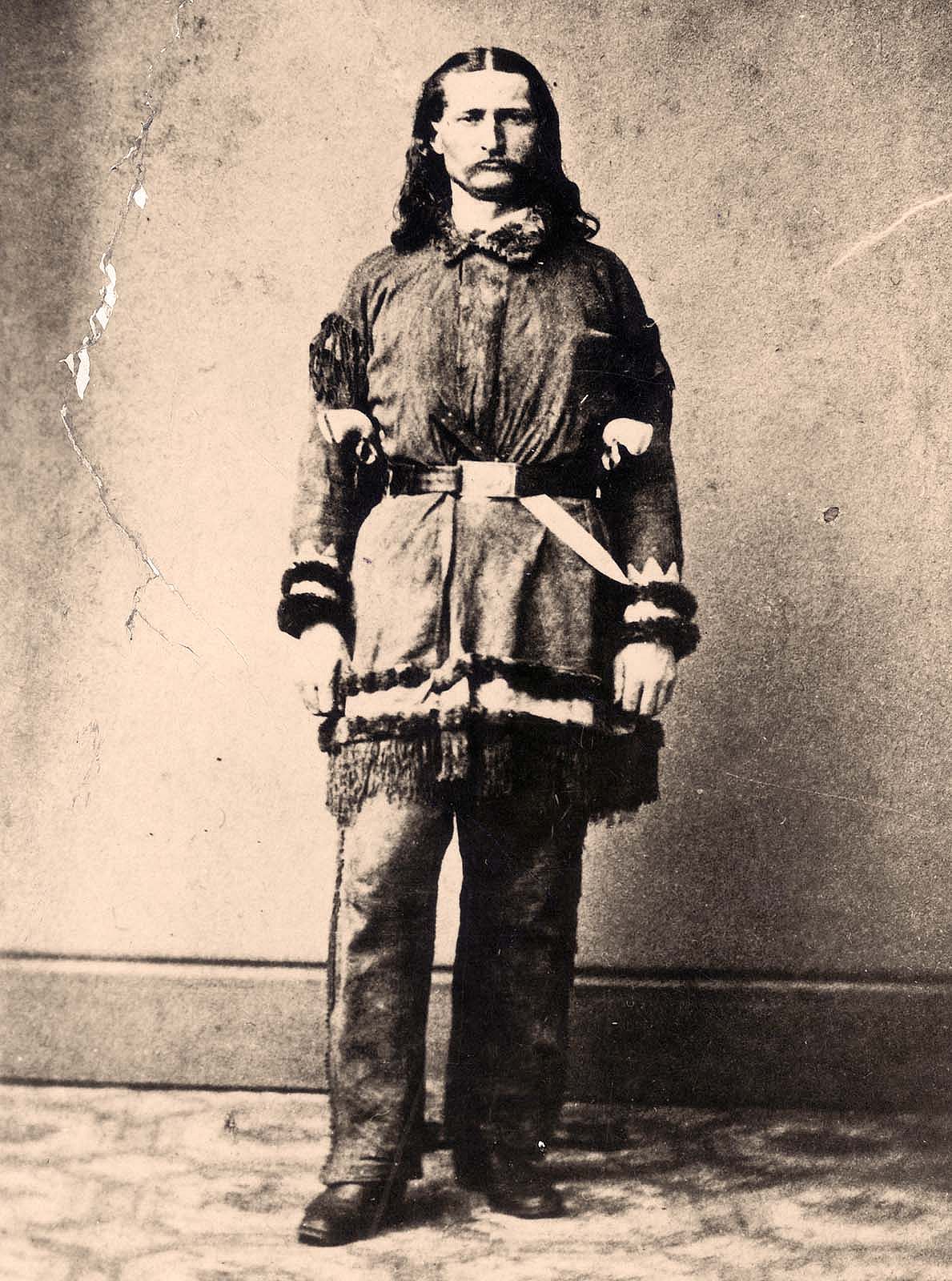 Portrait of James Butler “Wild Bill” Hickok wearing buckskin clothing and standing in front of wall. Knife tucked in belt. MS 71 Vincent Mercaldo Collection. P.71.475