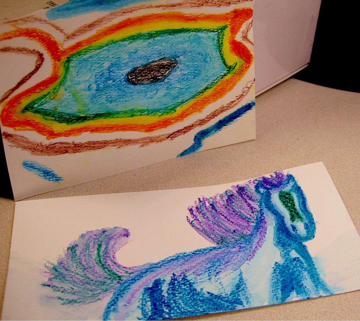 Children’s crayon artwork created during Family Fun Day at the Buffalo Bill Center, featuring a colorful abstract swirl and a playful blue horse drawing.