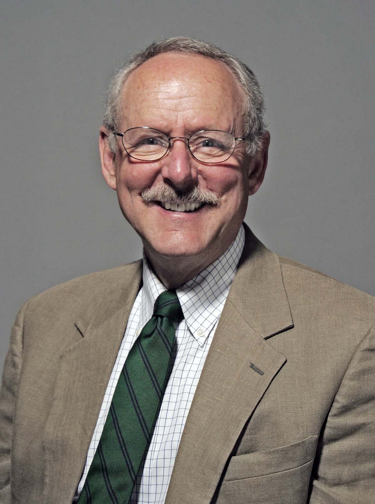 Peter Hassrick portrait with light gray background, wearing beige jacket and green/blue tie.