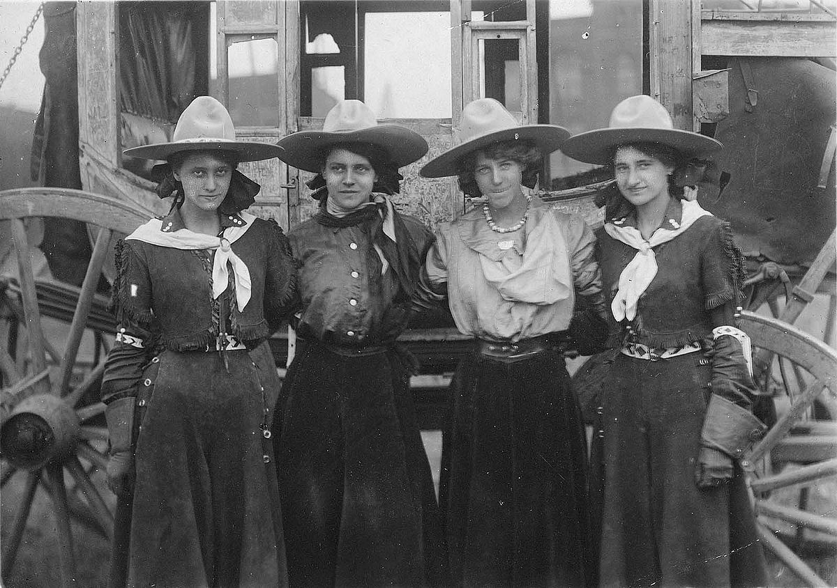 Four cowgirls posing in front of a stagecoach for the 101 Ranch Show, ca. 1916. Sepia toned photograph. MS 6 William F. Cody Collection, McCracken Research Library. P.69.1289