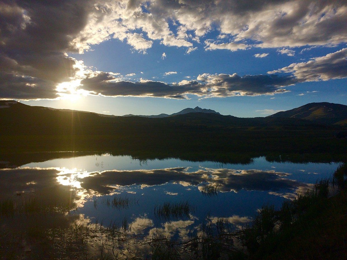 Scenic view of a sunset over a lake in Yellowstone National Park, with mountains and clouds reflecting on the water’s surface.