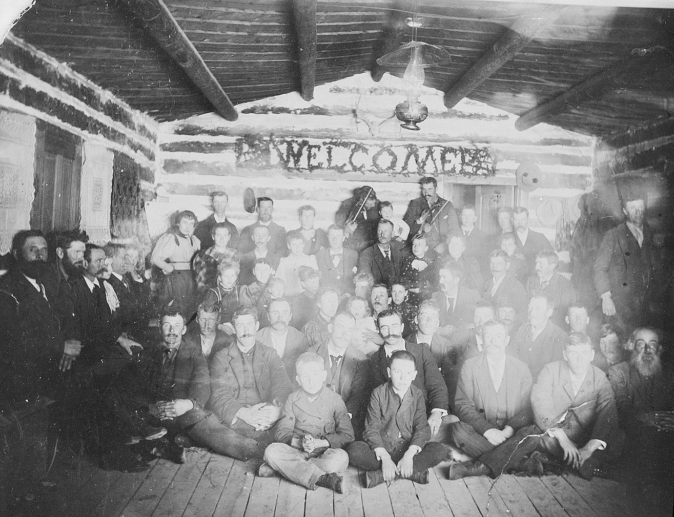 This group of people gathered under a "Welcome" sign in a log building in Wyoming in the early 1900s. We don’t know their names, or where the building stood. F.J. Hiscock photograph. MS89 Jack Richard Photograph Collection, McCracken Research Library. PN.89.18.3085.36