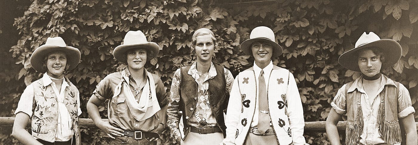 Five women dressed in western clothing in front of a hedge.