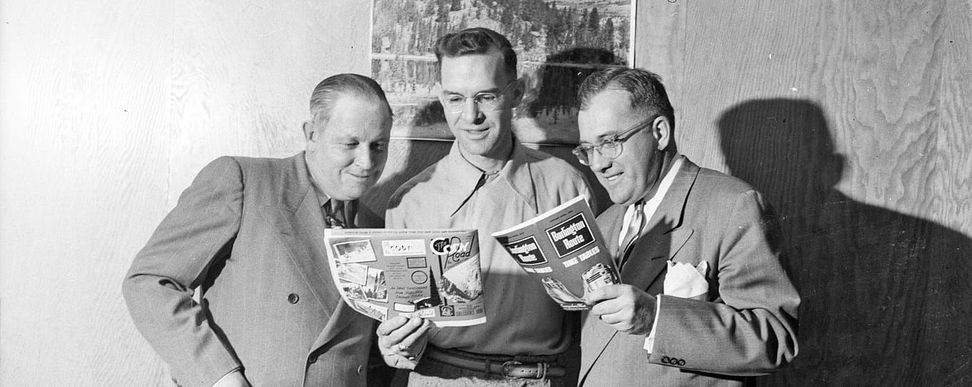 Three men reading magazines, center is Julius Alms of Burlington Railroad.