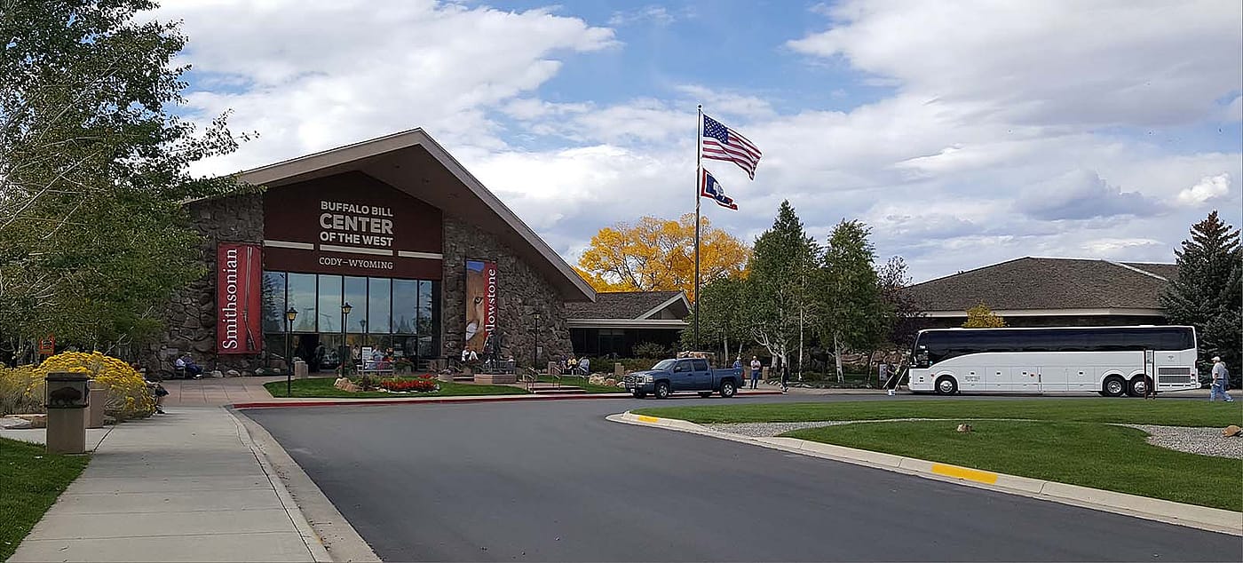 Buffalo Bill Center of the West entrance with a tour bus parked in front, set against a clear sky and welcoming visitors.
