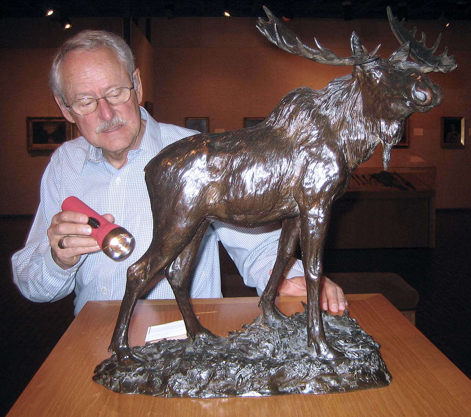 Peter Hassrick examining Henry Merwin Shrady's bronze sculpture "Bull Moose" with a flashlight.