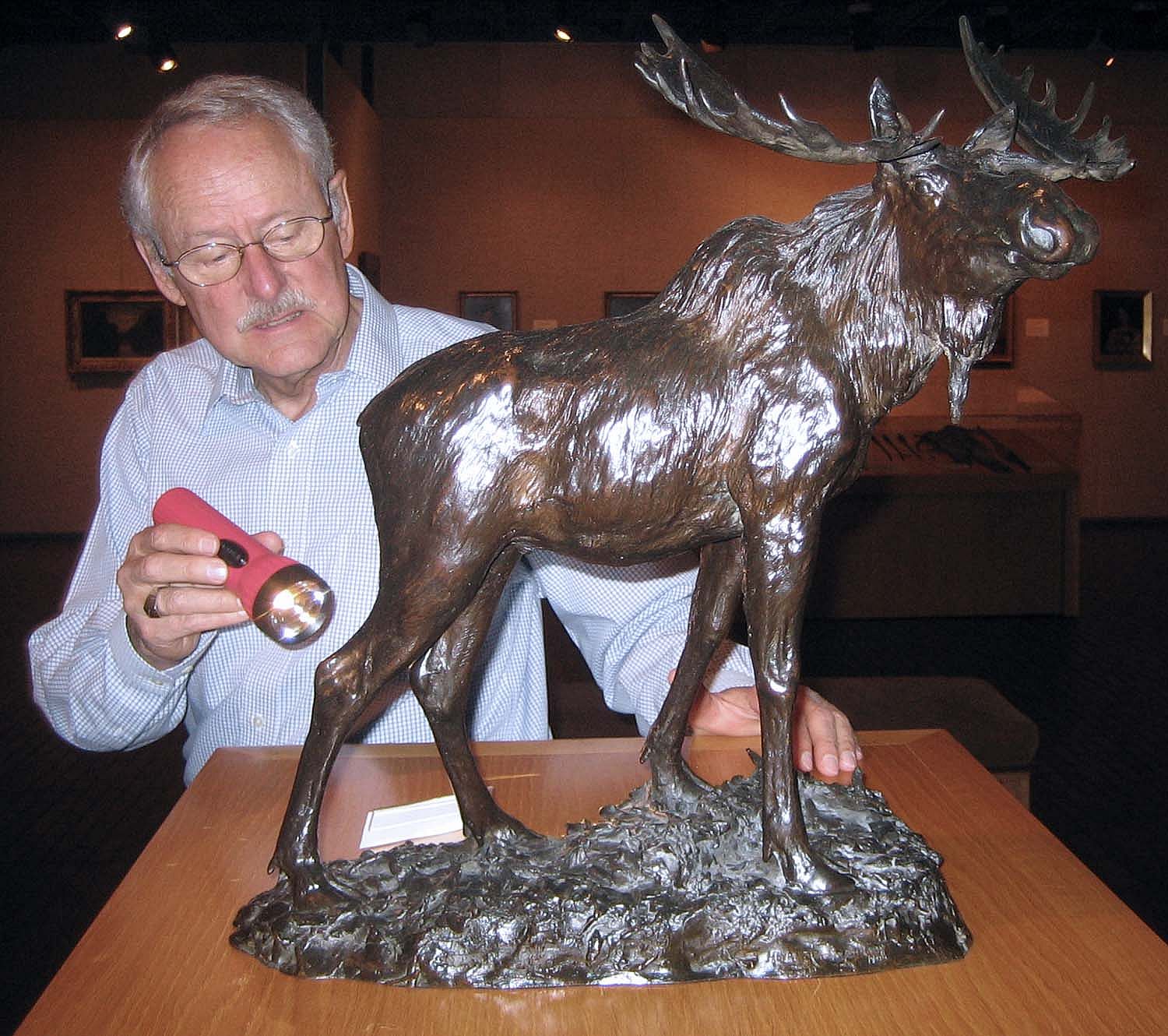 Peter Hassrick examining Henry Merwin Shrady's bronze sculpture "Bull Moose" with a flashlight.