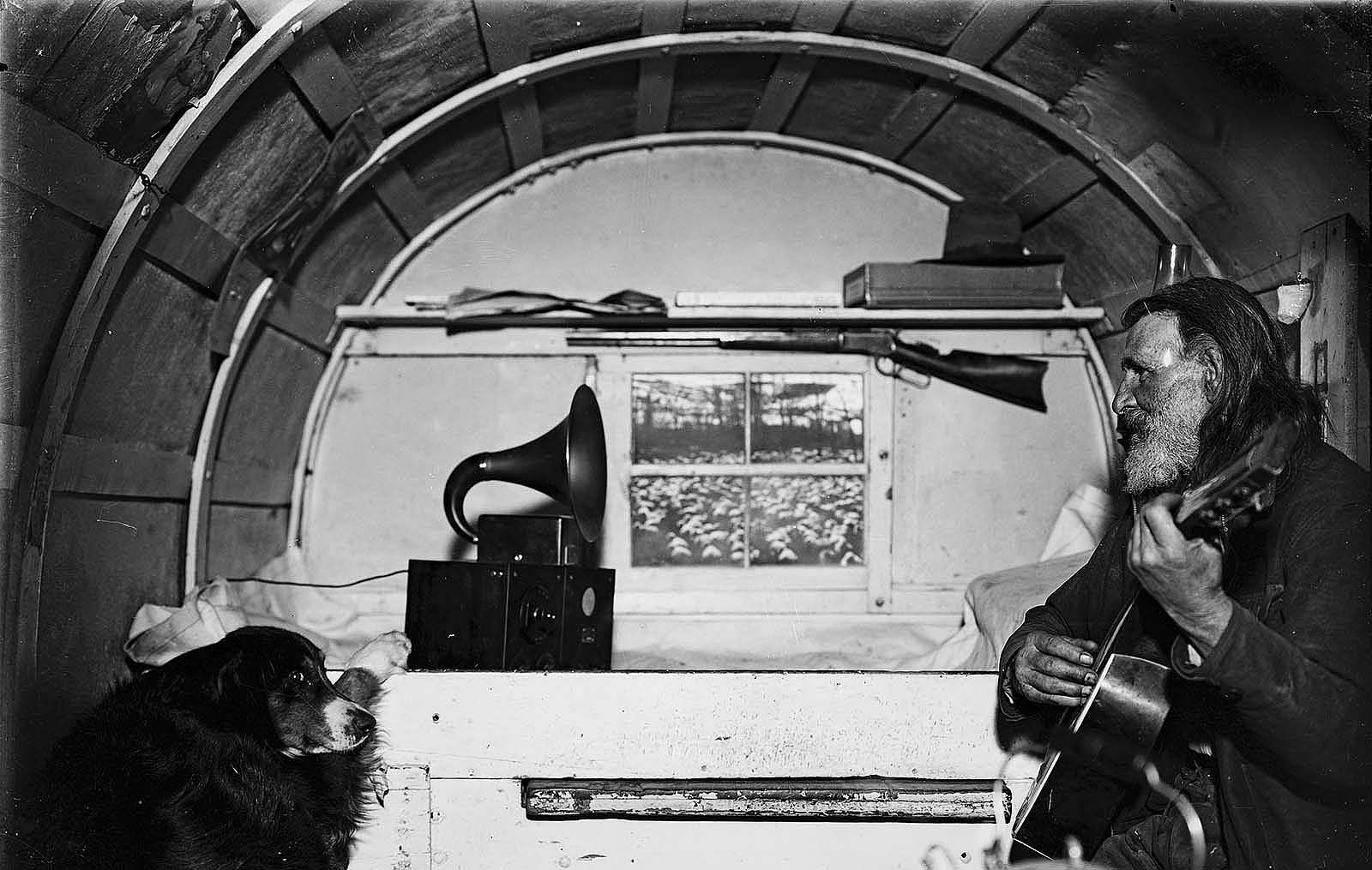 Sheepherder Jack Scott playing guitar in wagon with do, ca. 1930. Charles J. Belden photograph; glass plate negative. MS 3 Charles Belden Collection. PN.67.370 (detail)