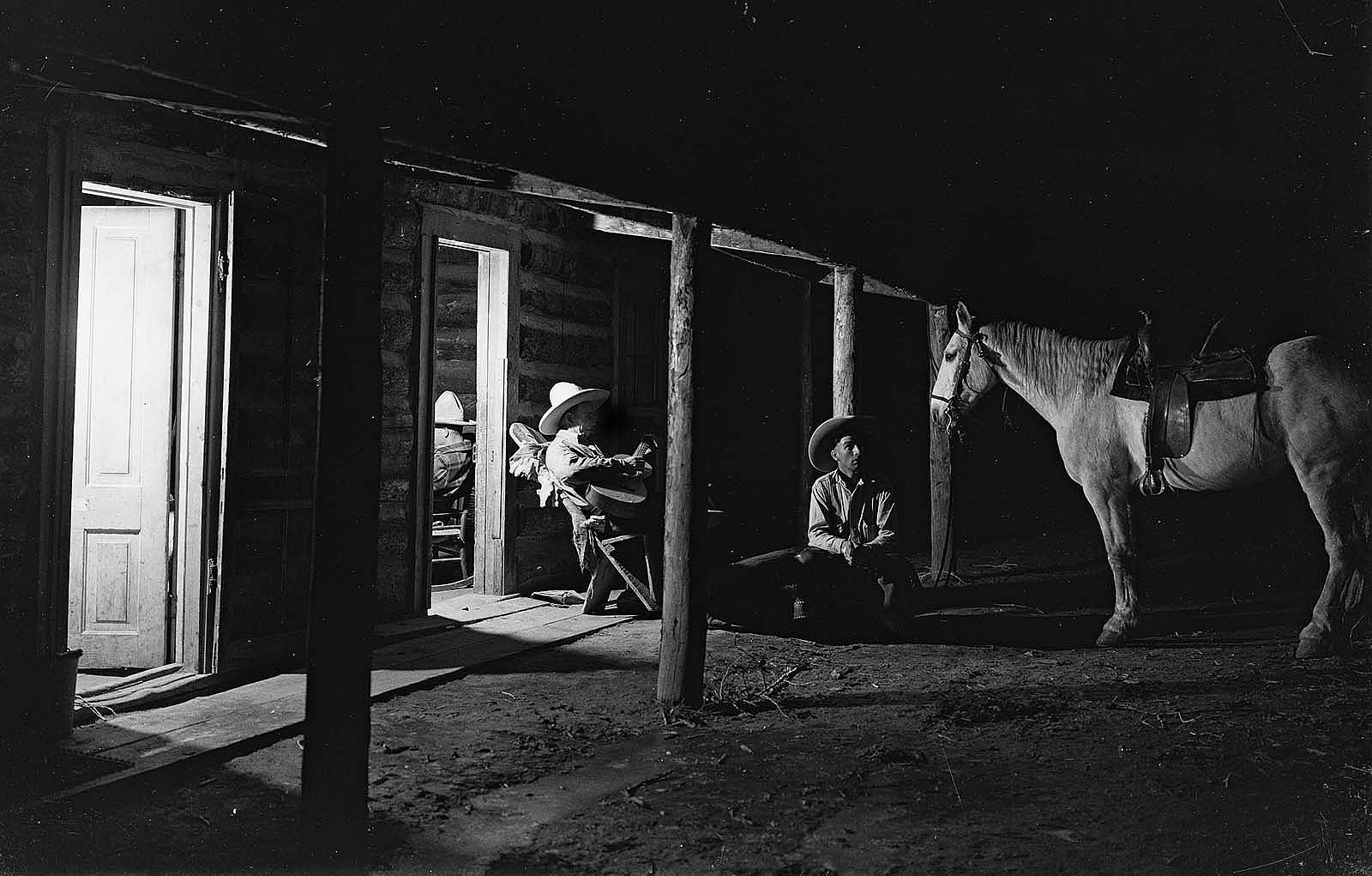 Cowboys sit in evening by bunkhouse on Pitchfork Ranch playing guitar. MS 3 Charles Belden Collection, McCracken Research Library. PN.67.025