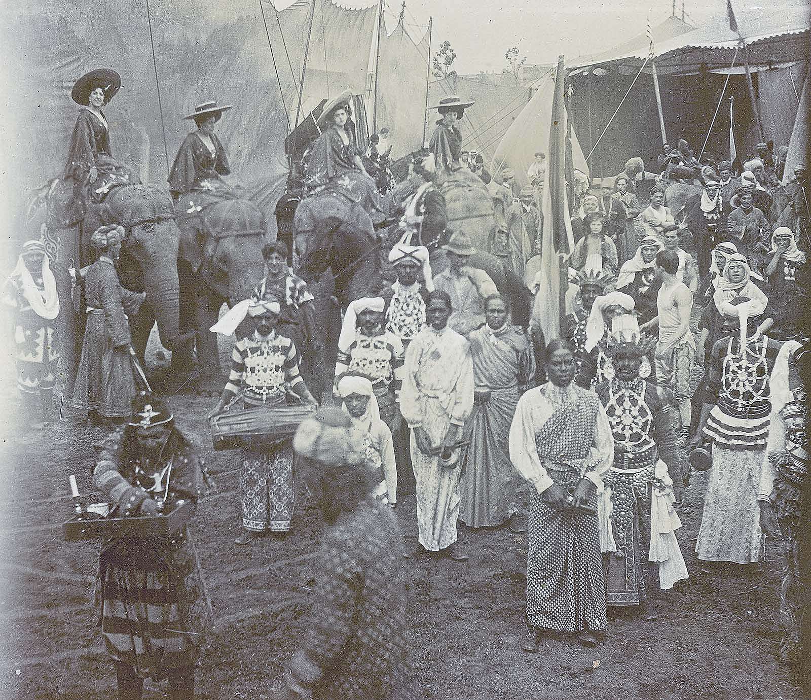 Black and white photo of cast members and four elephants in front of tents of "Far East" portion of Buffalo Bill's Wild West and Pawnee Bill's Far East show. MS6.4075.63.4
