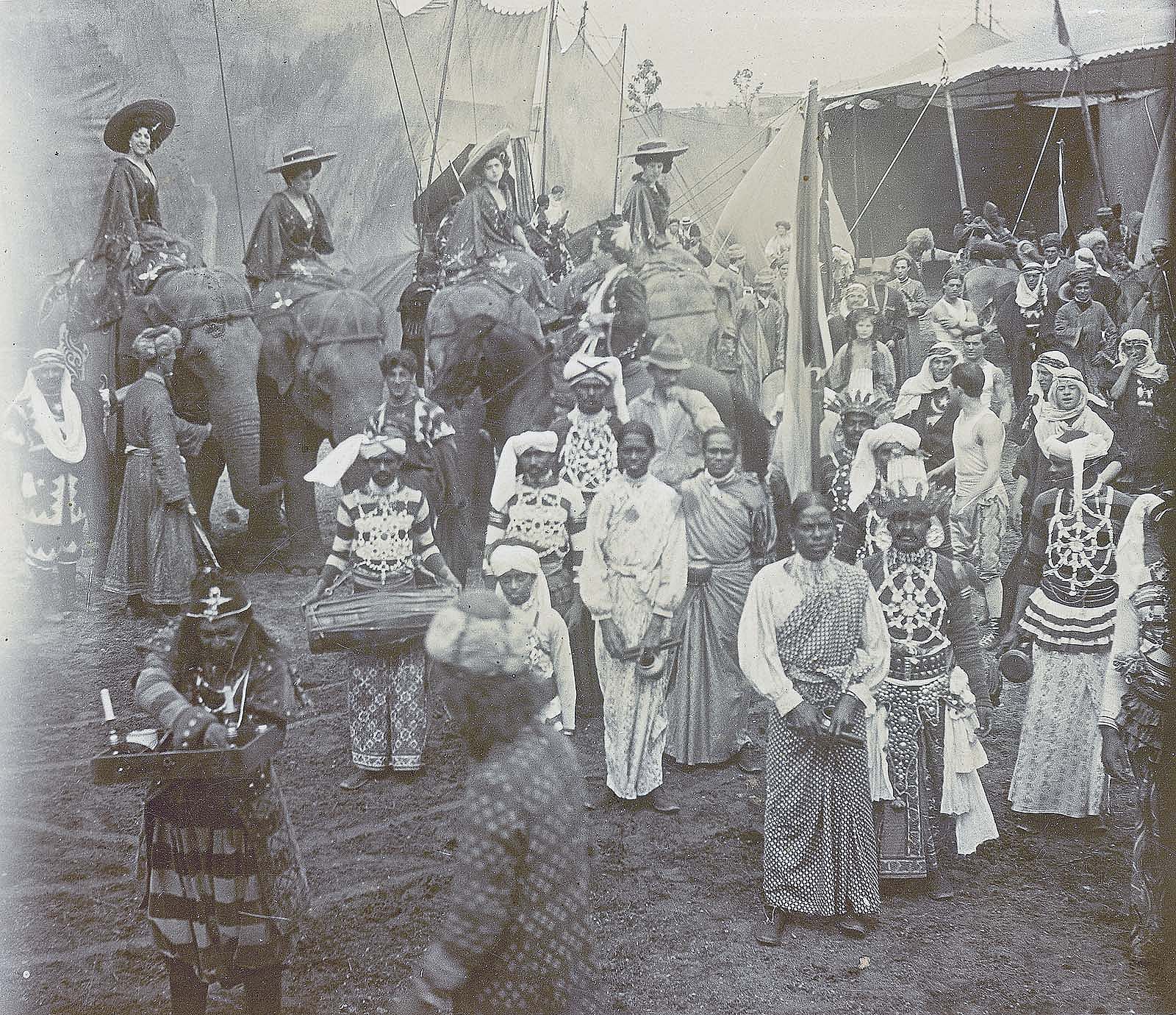 Black and white photo of cast members and four elephants in front of tents of "Far East" portion of Buffalo Bill's Wild West and Pawnee Bill's Far East show. MS6.4075.63.4