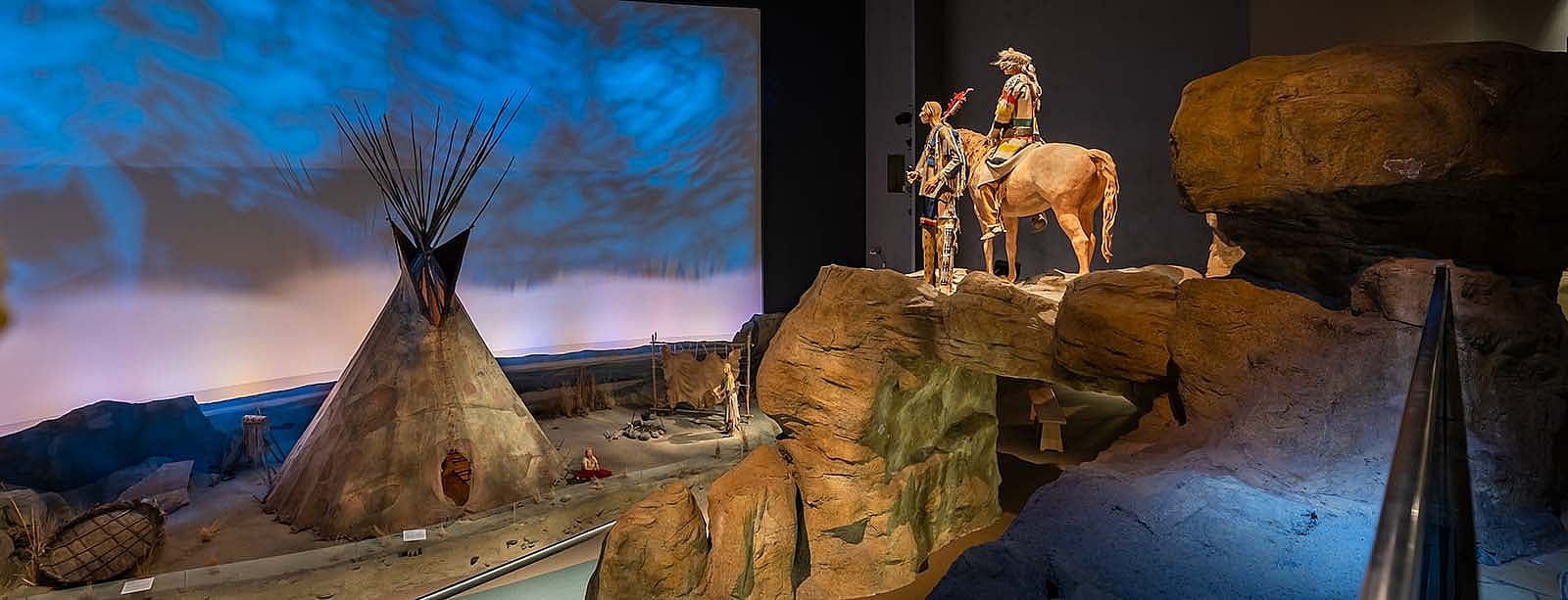 Plains Indian Museum, view of large hide tipi scene with horse and rider, and standing individual overlooking the scene.
