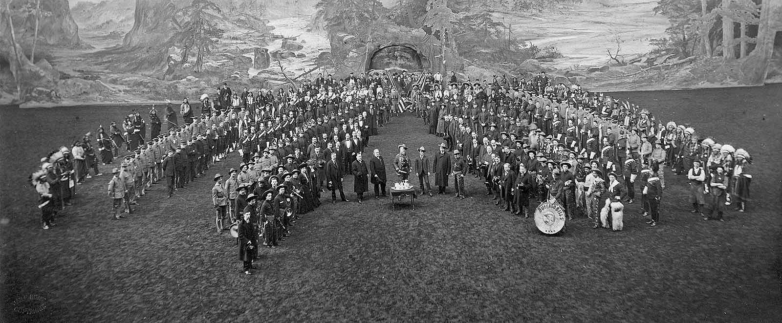 William F. Cody, center, and large group of Buffalo Bill's Wild West cast in show attire standing in formation in London, England. Type written note below photograph reads, "Buffalo Bill's Wild West Company's Presentation to their Chief on his Birthday at Olympia, London, Feb. 26,1903." P.69.1310c