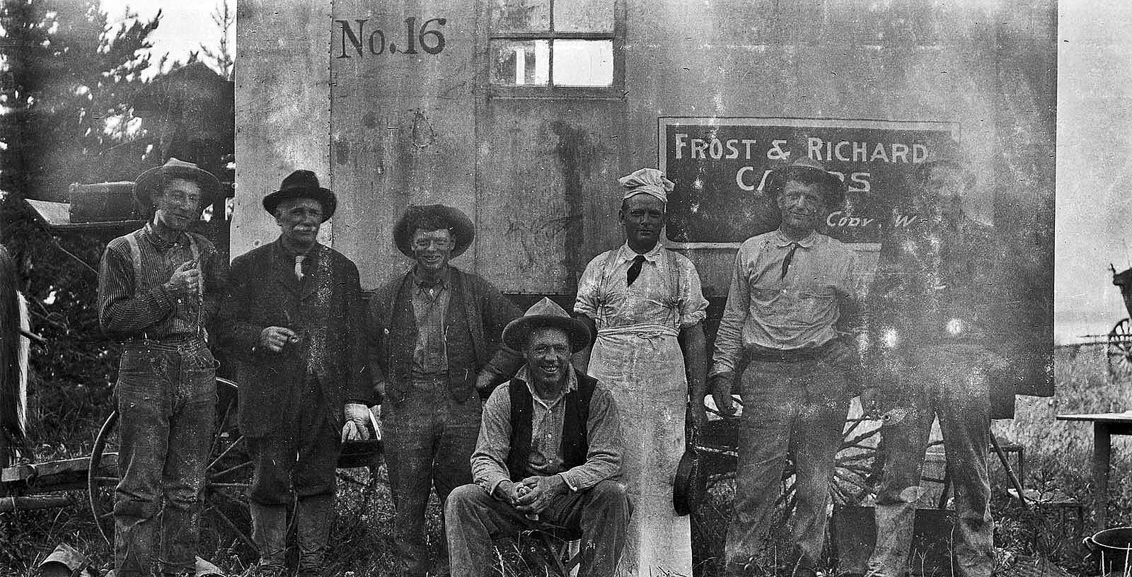The trail crew of a Frost & Richard tour. Ned Frost sitting on a stool in the center. Behind him on his left in white is “Phonograph” Jones, the camp cook. The smiling man over Ned’s right shoulder is “Shorty” Kelly, Ned’s top hand. I don’t know who the others are, packers and drivers.