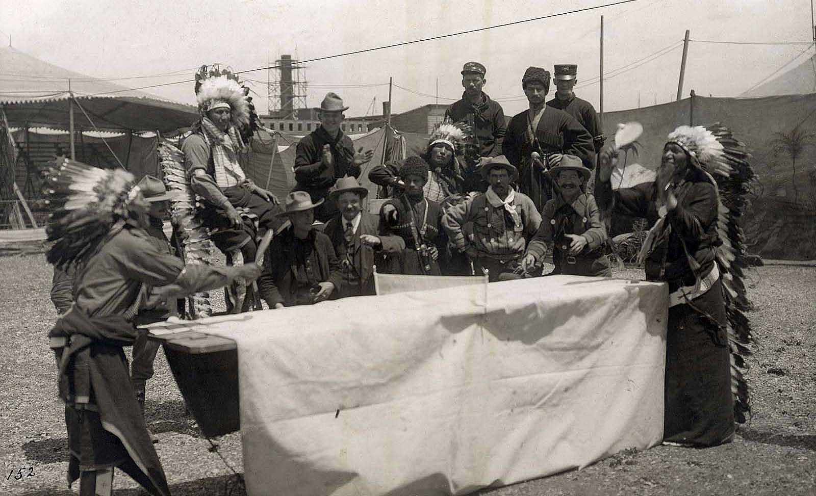 A performer who may be Oglala Lakota Chief Iron Tail plays ping pong with a fellow castmate as Joe Black Fox and a group Native performers, cowboys, vaqueros, and Cossacks watch the match. MS 6 William F. Cody Collection, McCracken Research Library. P.69.1033