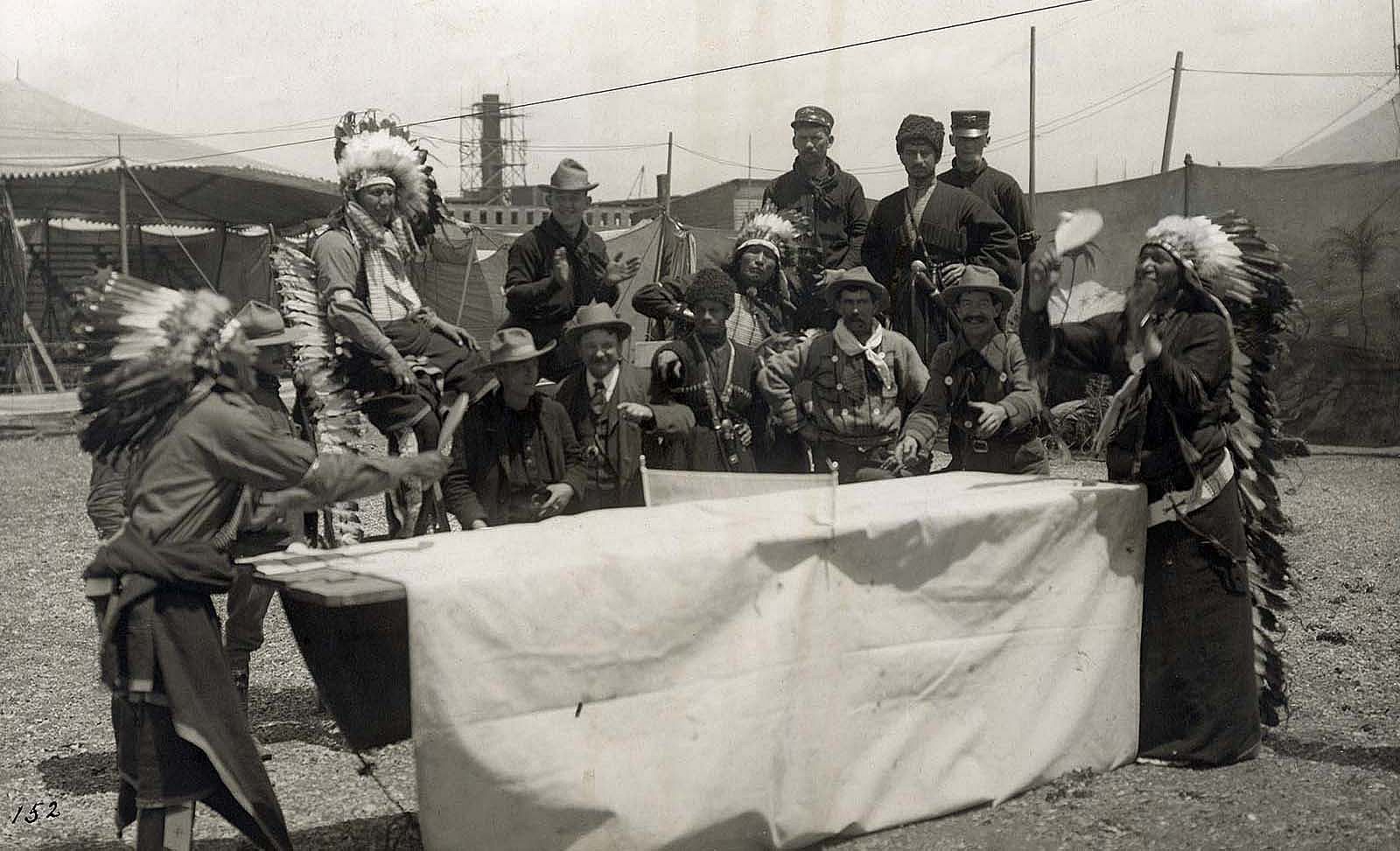 A performer who may be Oglala Lakota Chief Iron Tail plays ping pong with a fellow castmate as Joe Black Fox and a group Native performers, cowboys, vaqueros, and Cossacks watch the match. MS 6 William F. Cody Collection, McCracken Research Library. P.69.1033