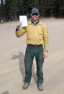 Beau Kidd, in forest green pants and yellow shirt, holds up kid's drawing.