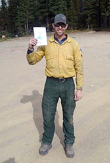 Beau Kidd, in forest green pants and yellow shirt, holds up kid's drawing.