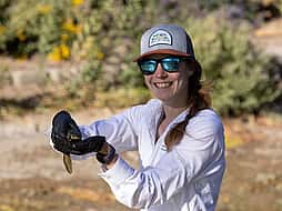 Amy Phillips outdoors in cap and wearing sunglasses, holding a tiger salamander. Julia Cook photo, 2024.