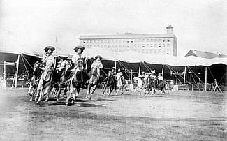 Etheyle Parry and Juanita Parry lead cowgirls riding horses around the Buffalo Bill's Wild West arena. MS 6 William F. Cody Collection, McCracken Research Library. P.69.1304
