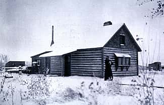 Absarokee Hut in winter, ca. 1905. Addie Sharp stands on the front walk, holding her dog Frans Hals. P. 22.523