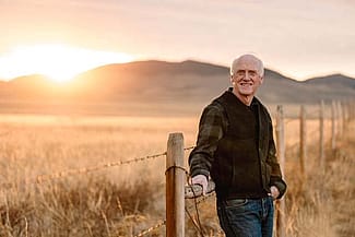 Dr. John Squires, casual outdoor photo by a fence with mountains in background and golden light.