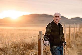 Dr. John Squires, casual outdoor photo by a fence with mountains in background and golden light.