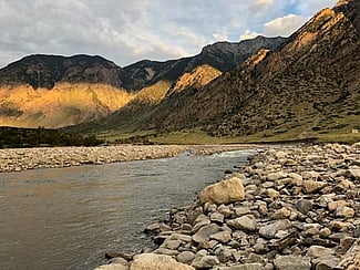 Mountains in background with river and river rock in foreground. Photo by George Miller.