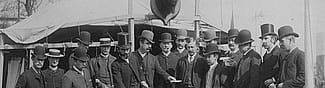 Black and white photograph. Group of men in hats and suits at Buffalo Bill's Wild West gather in front of William F. Cody's tent on Buffalo Bill's Wild West show backlot. Elliot & Fry, Baker Street, London, photographer. William F. Cody Collection. P.69.810 (detail)