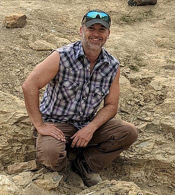 Paleontologist Jason Schein in the field, sitting next to excavations.