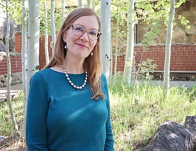 Amy Sullivan in aqua shirt, outside in garden with trees.