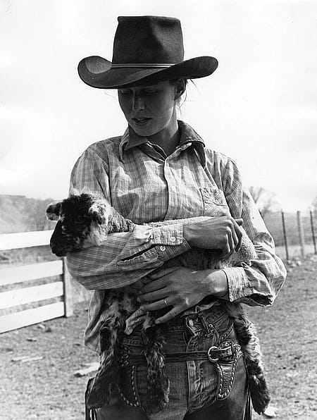 Woman in cowboy hat holding a lamb. James Bama (1926 – 2022), Dede Fales, Antlers Ranch, 1976. Black and white photograph, 14 x 11 inches. Buffalo Bill Center of the West, Cody, WY. MS 243 James Bama Collection, McCracken Research Library. P.243.02473