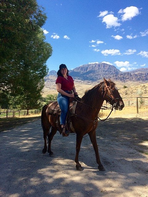 Person horseback riding on a scenic trail in Wyoming, with mountains and trees in the background.