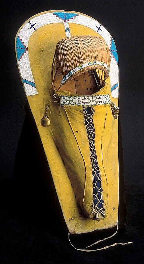 Cradle, late 1800s. Ute, Southern Colorado or Utah. Tanned deer hide, wood, willow, glass beads, pigments, brass, cowrie shells. Gift of Corliss C. and Audrienne H. Moseley. NA.111.19