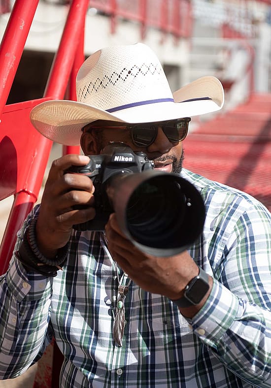 Man in cowboy hat with camera and large lens.