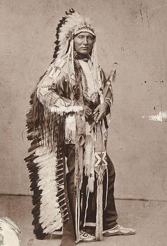 Black and white postcard. Touch the Clouds wearing war bonnet and traditional regalia. Photo attributed to Julius Ulke. The Paul Dyck Plains Indian Buffalo Culture Collection, acquired through the generosity of the Dyck family and additional gifts of the Nielson Family and the Estate of Margaret S. Coe. P.320.429