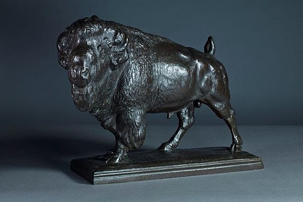 Bronze sculpture of a bison standing on a rectangular base, showcasing detailed musculature and textured fur against a dark background.