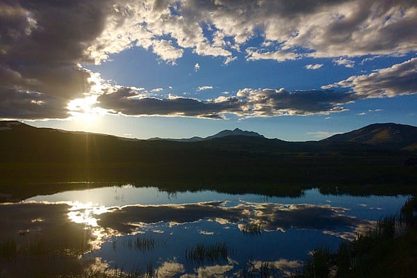Scenic view of a sunset over a lake in Yellowstone National Park, with mountains and clouds reflecting on the water’s surface.