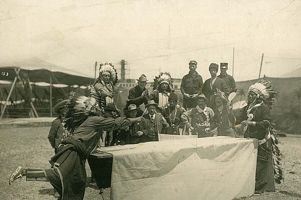 A performer who may be Oglala Lakota Chief Iron Tail plays ping pong with a fellow castmate as Joe Black Fox and a group Native performers, cowboys, vaqueros, and Cossacks watch the match. MS 6 William F. Cody Collection, McCracken Research Library. P.69.1031