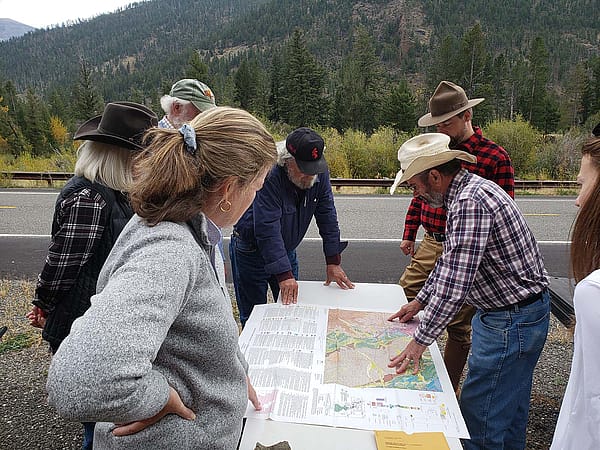 Geology field trip participants gather around as an instructor reads a map.